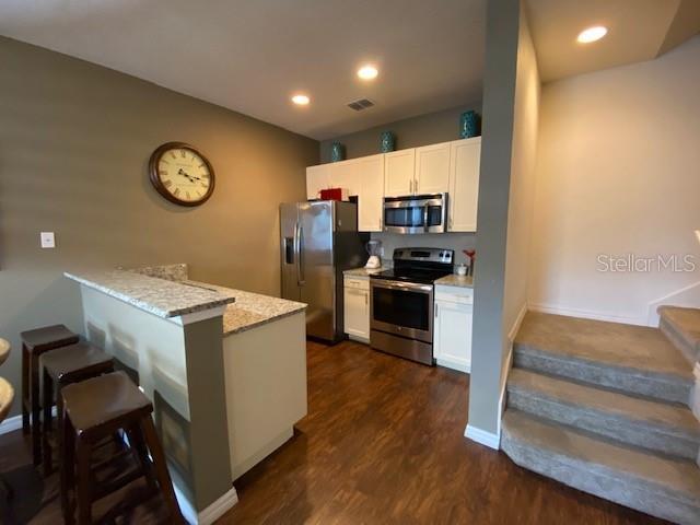 5370 Diplomat Ct Unit 107, Kissimmee, FL 34746 - kitchen with stainless steel appliances, a breakfast bar, white cabinetry, a peninsula, and dark wood-type flooring