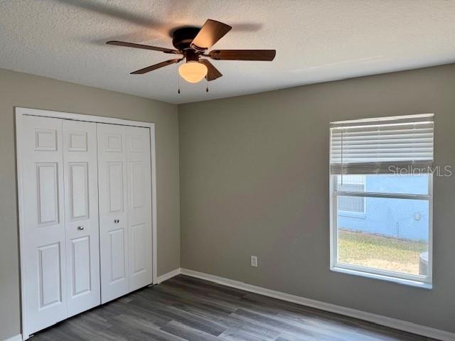 307 Dalton Ct, Davenport, FL 33897 - unfurnished bedroom with dark wood-style flooring, a closet, baseboards, a ceiling fan, and a textured ceiling