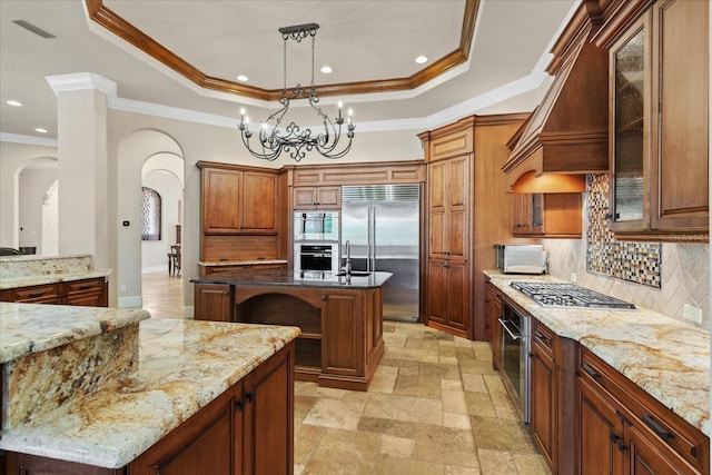 9253 Tibet Pointe Cir, Windermere, FL 34786 - kitchen featuring appliances with stainless steel finishes, arched walkways, a tray ceiling, an island with sink, and light stone counters