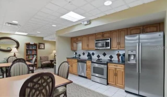 400 E Colonial Dr Unit 910, Orlando, FL 32803 - kitchen with appliances with stainless steel finishes, a paneled ceiling, dark countertops, brown cabinets, and light tile patterned flooring