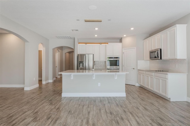 1740 Standing Rock Cir, Oakland, FL 34787 - kitchen featuring appliances with stainless steel finishes, a kitchen island with sink, decorative backsplash, light wood-style flooring, and white cabinetry