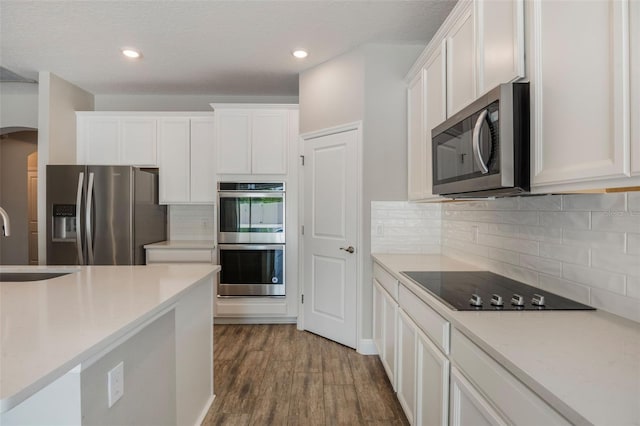 1740 Standing Rock Cir, Oakland, FL 34787 - kitchen with stainless steel appliances, arched walkways, white cabinets, wood finished floors, and tasteful backsplash
