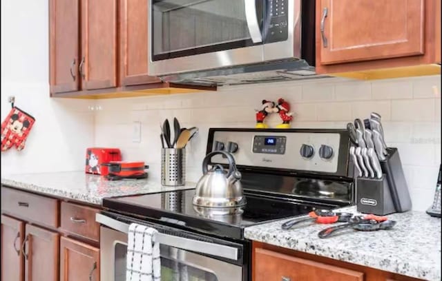 1625 Nassau Point Trl, Kissimmee, FL 34747 - kitchen with stainless steel appliances, backsplash, brown cabinets, and light stone countertops