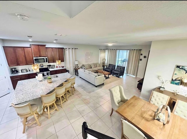 1625 Nassau Point Trl, Kissimmee, FL 34747 - kitchen featuring stainless steel appliances, light tile patterned floors, a kitchen bar, a kitchen island, and light stone counters