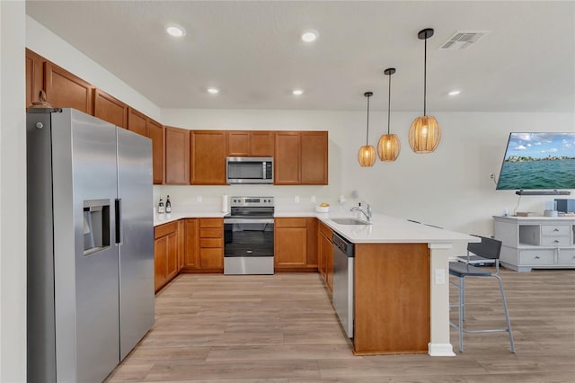 14335 Sapelo Beach Dr, Orlando, FL 32827 - kitchen with appliances with stainless steel finishes, a peninsula, light wood-style flooring, brown cabinetry, and recessed lighting