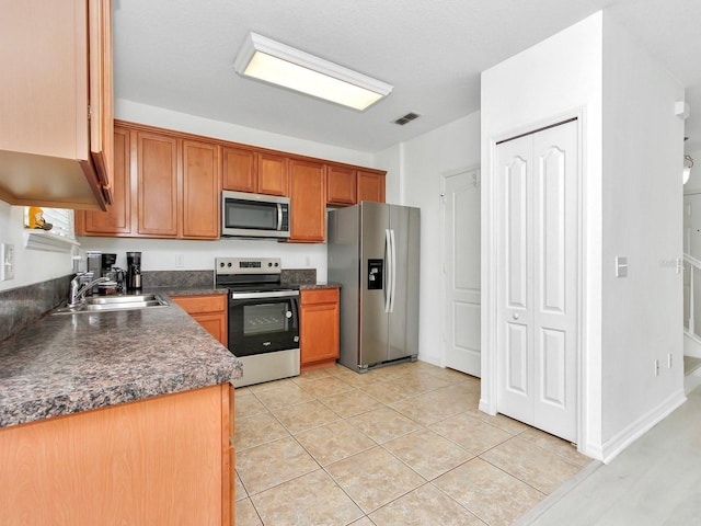2311 Chatham Place Dr, Orlando, FL 32824 - kitchen with appliances with stainless steel finishes, dark countertops, a sink, brown cabinets, and light tile patterned flooring