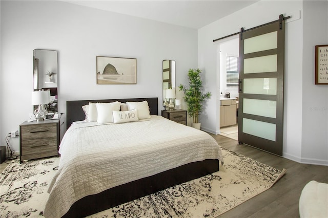 95353 Orchid Blossom Trl, Fernandina Beach, FL 32034 - bedroom with a barn door, wood finished floors, baseboards, and ensuite bath