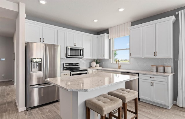 1811 Spring Shower Cir, Kissimmee, FL 34744 - kitchen with stainless steel appliances, a kitchen island, white cabinetry, a kitchen bar, and light wood-style flooring