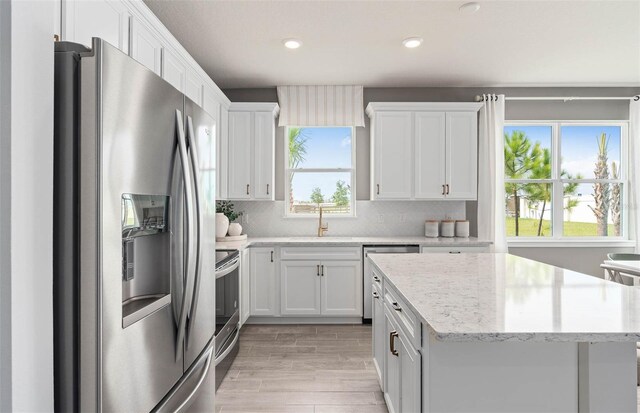 1811 Spring Shower Cir, Kissimmee, FL 34744 - kitchen featuring appliances with stainless steel finishes, white cabinetry, light wood finished floors, a kitchen island, and backsplash