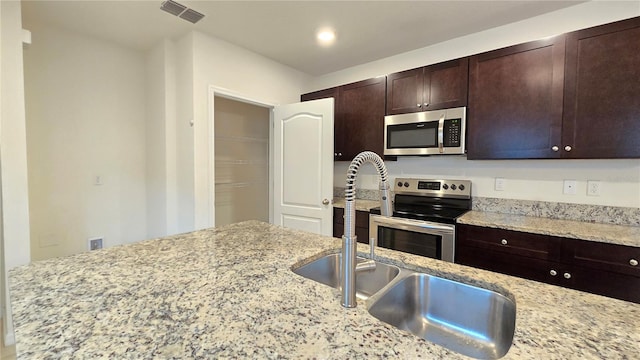 3202 Timber Hawk Cir, Ocoee, FL 34761 - kitchen with stainless steel appliances, dark brown cabinets, a sink, light stone counters, and recessed lighting
