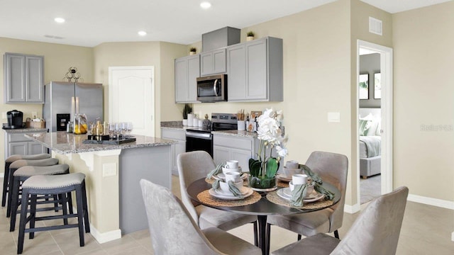 4932 Kaia Ave, Winter Haven, FL 33884 - kitchen featuring stainless steel appliances, gray cabinetry, a center island with sink, light stone countertops, and a kitchen bar