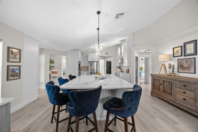 1301 Johns Cove Ln, Oakland, FL 34787 - kitchen with freestanding refrigerator, white cabinets, light wood-style floors, a kitchen bar, and vaulted ceiling