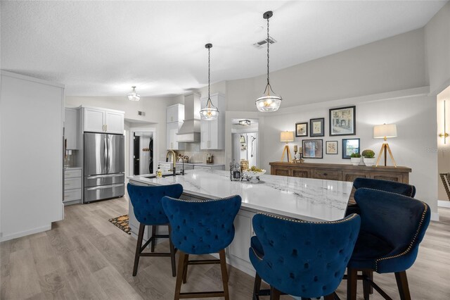 1301 Johns Cove Ln, Oakland, FL 34787 - kitchen featuring freestanding refrigerator, wall chimney range hood, a kitchen bar, white cabinetry, and light wood-type flooring
