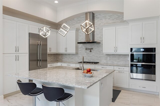 8113 Via Vittoria Way, Orlando, FL 32819 - kitchen with appliances with stainless steel finishes, wall chimney exhaust hood, light marble finish flooring, an island with sink, and ornamental molding