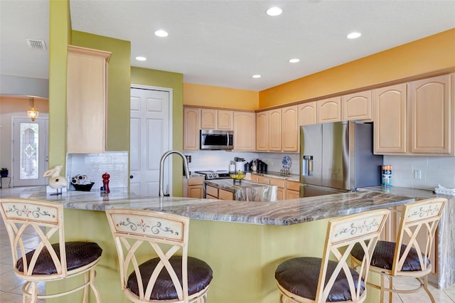 2631 Captains Ct, Kissimmee, FL 34746 - kitchen featuring stainless steel appliances, light brown cabinetry, a peninsula, backsplash, and a kitchen bar