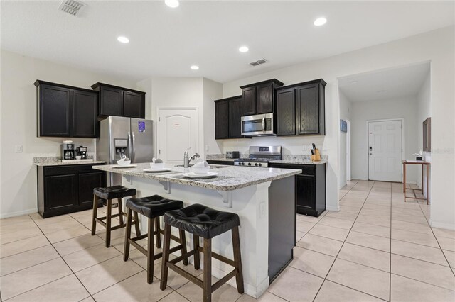 7033 Oakwood St, Davenport, FL 33837 - kitchen with appliances with stainless steel finishes, light tile patterned flooring, a breakfast bar, dark cabinetry, and recessed lighting