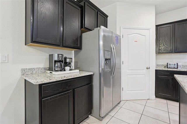 7033 Oakwood St, Davenport, FL 33837 - kitchen featuring stainless steel refrigerator with ice dispenser, light tile patterned flooring, dark cabinetry, and light stone countertops