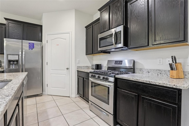 7033 Oakwood St, Davenport, FL 33837 - kitchen featuring stainless steel appliances, light tile patterned floors, light stone counters, and dark cabinets