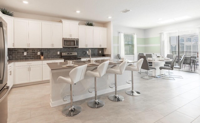 8986 Cabot Cliffs Dr, Davenport, FL 33896 - kitchen with stainless steel appliances, decorative backsplash, a center island with sink, a kitchen bar, and white cabinetry