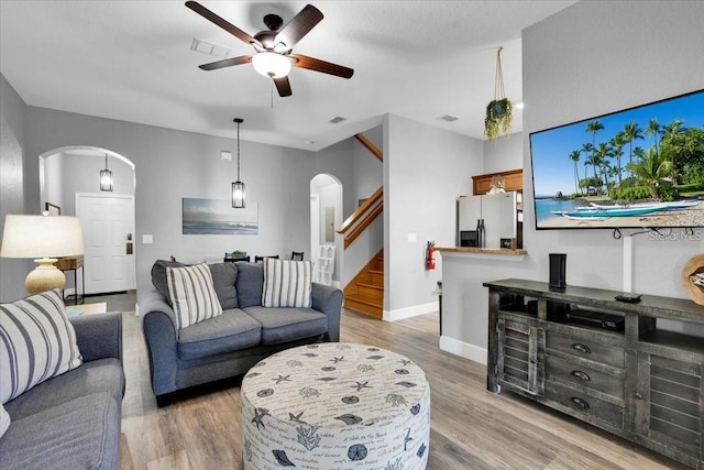 3214 Calabria Ave, Davenport, FL 33897 - living room featuring arched walkways, ceiling fan, stairs, light wood finished floors, and baseboards