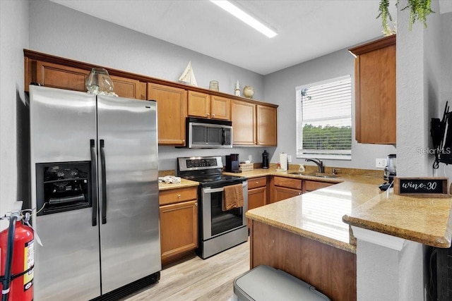 3214 Calabria Ave, Davenport, FL 33897 - kitchen with appliances with stainless steel finishes, a sink, a peninsula, light wood finished floors, and brown cabinets