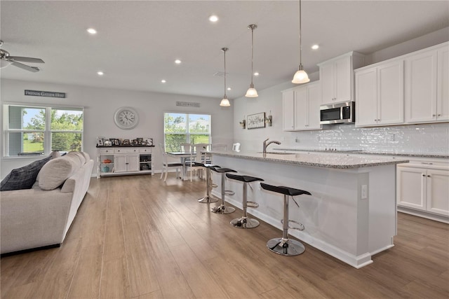 2168 Aibonito Cir, Clermont, FL 34711 - kitchen featuring stainless steel microwave, open floor plan, white cabinetry, tasteful backsplash, and wood finished floors