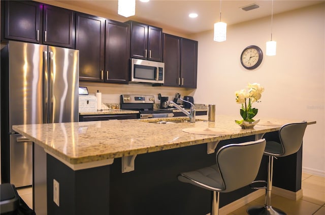 130 Claire Ln, Davenport, FL 33837 - kitchen with appliances with stainless steel finishes, a kitchen bar, light stone countertops, decorative light fixtures, and an island with sink