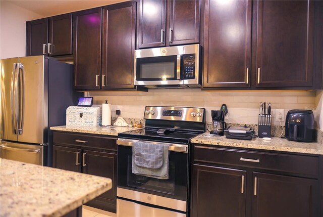 130 Claire Ln, Davenport, FL 33837 - kitchen with stainless steel appliances, backsplash, light stone countertops, and dark brown cabinetry