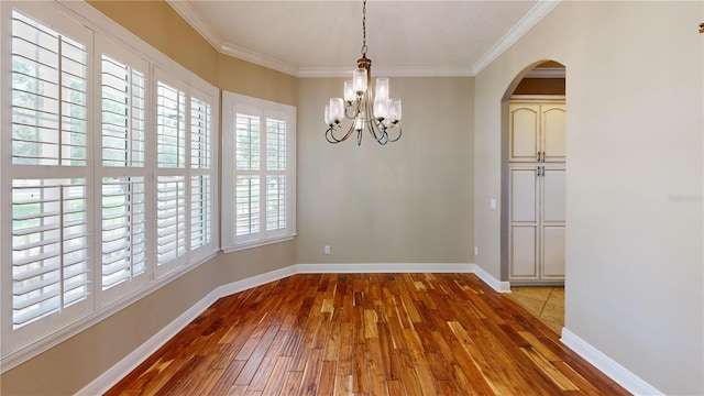 10809 Arrowtree Blvd, Clermont, FL 34715 - unfurnished dining area with wood-type flooring, a chandelier, ornamental molding, baseboards, and arched walkways