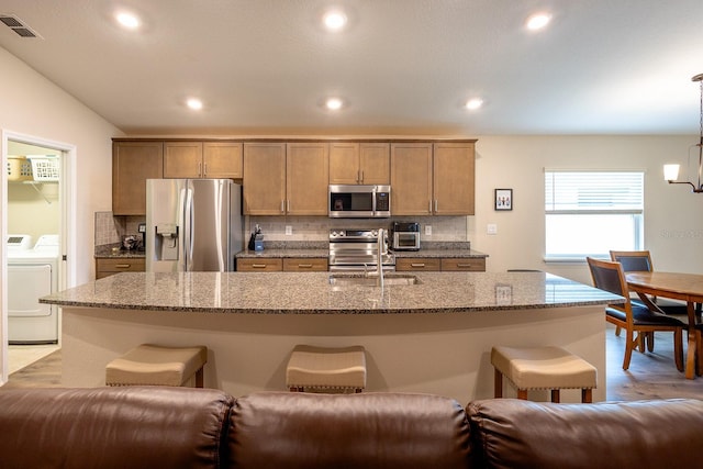 5416 Tessin Trl, Saint Cloud, FL 34771 - kitchen featuring appliances with stainless steel finishes, independent washer and dryer, a sink, a breakfast bar, and tasteful backsplash