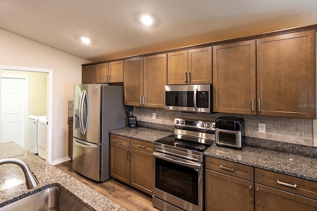 5416 Tessin Trl, Saint Cloud, FL 34771 - kitchen with appliances with stainless steel finishes, washer and dryer, a sink, wood finished floors, and decorative backsplash