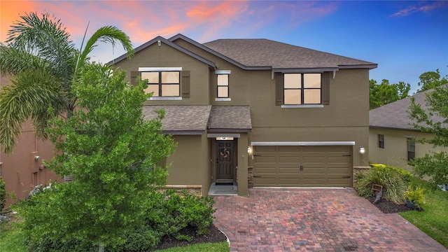 traditional-style house with stucco siding, a garage, decorative driveway, and a shingled roof