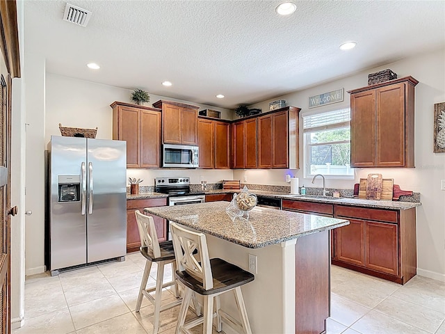 kitchen with appliances with stainless steel finishes, a sink, light stone countertops, light tile patterned floors, and a textured ceiling