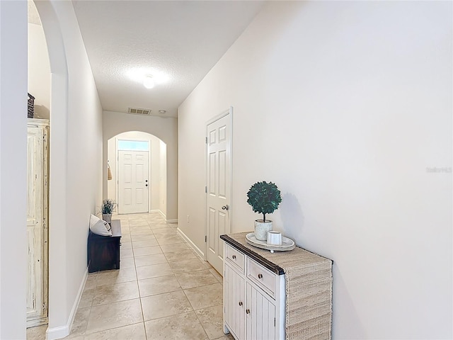 corridor featuring arched walkways, light tile patterned flooring, a textured ceiling, and baseboards