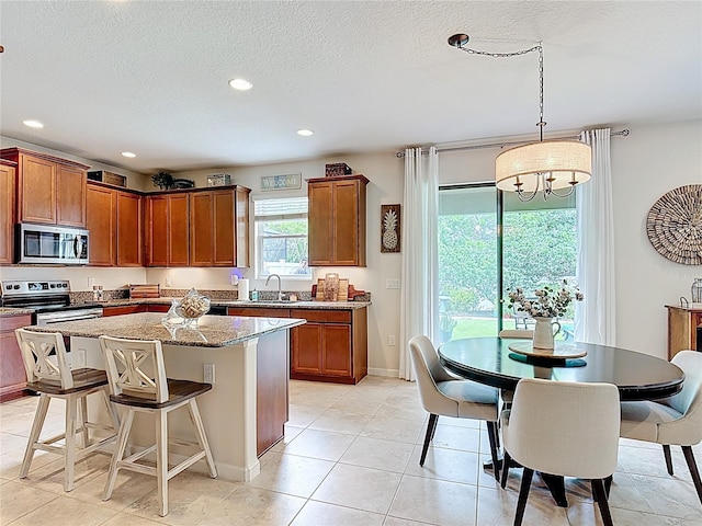 kitchen featuring stainless steel appliances, a sink, a kitchen island, a textured ceiling, and light stone counters