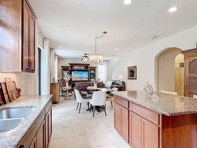 kitchen with arched walkways, open floor plan, light stone countertops, hanging light fixtures, and recessed lighting