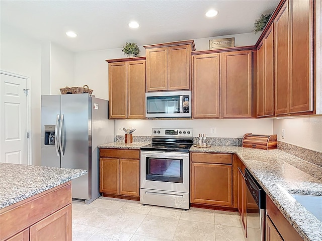 kitchen with stainless steel appliances, light stone countertops, brown cabinetry, and recessed lighting
