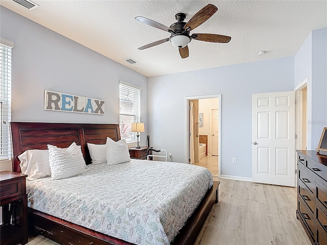 bedroom featuring light wood-style floors, a textured ceiling, connected bathroom, ceiling fan, and baseboards