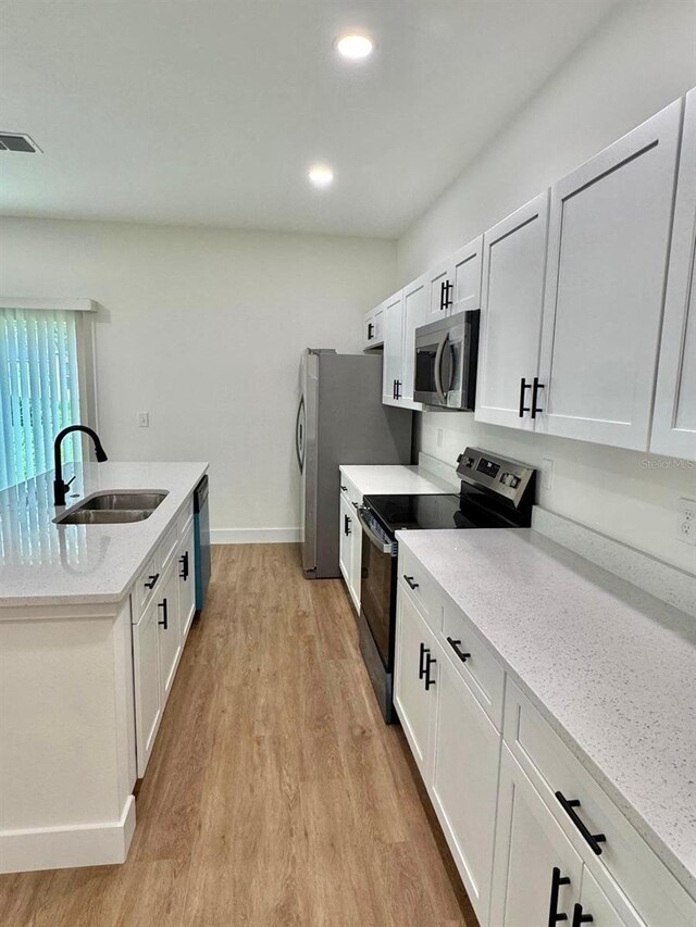 319 Anchovie Ct, Poinciana, FL 34759 - kitchen featuring appliances with stainless steel finishes, a sink, light wood-type flooring, an island with sink, and white cabinetry