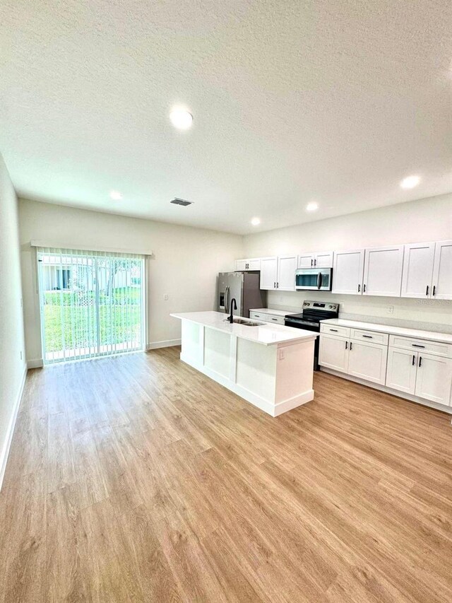 319 Anchovie Ct, Poinciana, FL 34759 - kitchen featuring stainless steel appliances, light wood-style floors, a textured ceiling, a sink, and a center island with sink