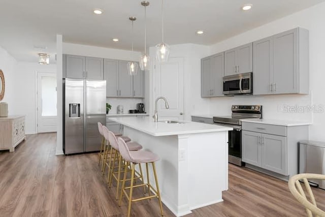 2363 Lancashire St, Davenport, FL 33896 - kitchen with appliances with stainless steel finishes, gray cabinetry, a sink, wood finished floors, and a kitchen island with sink