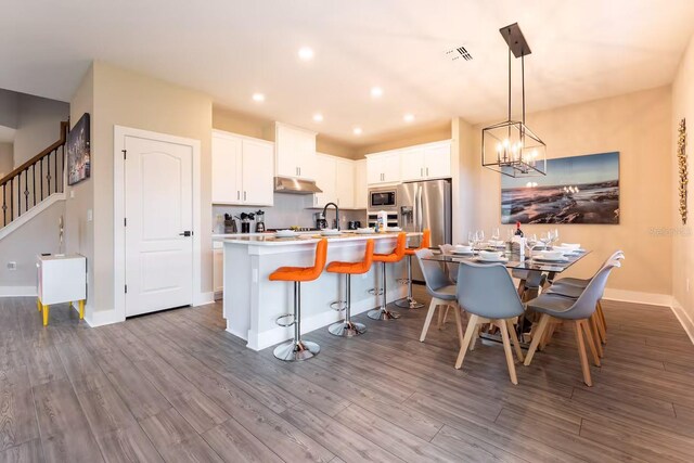7951 Haverhill Way, Kissimmee, FL 34747 - kitchen with under cabinet range hood, dark wood-type flooring, a kitchen bar, appliances with stainless steel finishes, and light countertops