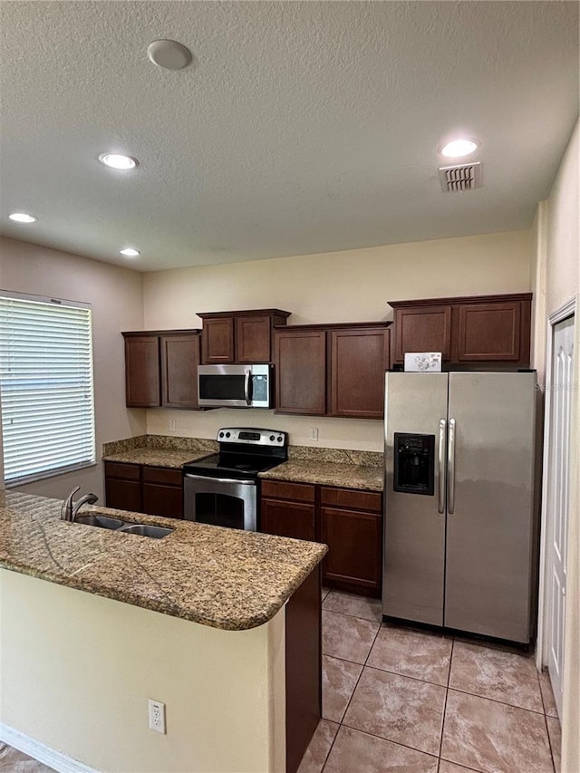 11187 Savannah Landing Cir, Orlando, FL 32832 - kitchen with appliances with stainless steel finishes, a sink, dark brown cabinets, stone counters, and a textured ceiling