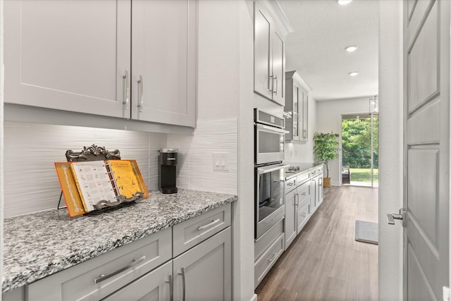 2340 Standing Rock Cir, Oakland, FL 34787 - kitchen with backsplash, gray cabinets, wood finished floors, stainless steel double oven, and light stone countertops