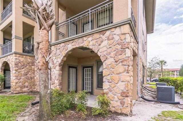 909 Charo Pkwy Unit 1011, Davenport, FL 33897 - view of exterior entry with stone siding, central AC, stucco siding, and a balcony