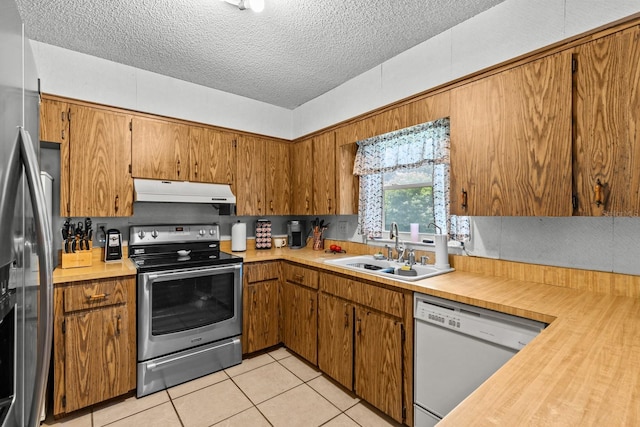 310 E Gulley Ave, Oakland, FL 34760 - kitchen with stainless steel appliances, under cabinet range hood, a sink, light tile patterned floors, and brown cabinets