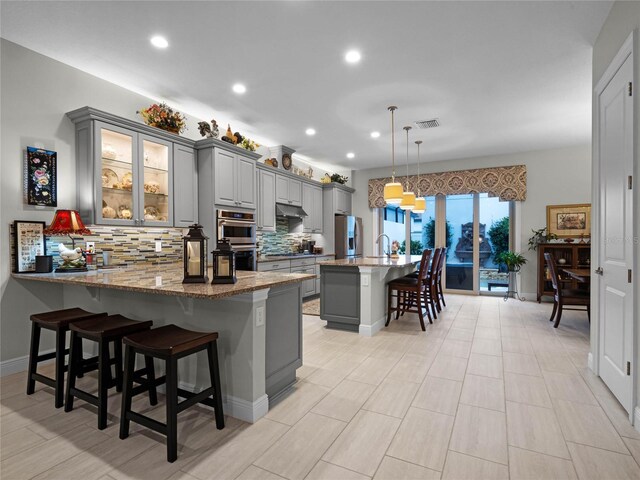 8818 Bismarck Palm Dr, Winter Garden, FL 34787 - kitchen with gray cabinets, stainless steel appliances, under cabinet range hood, a breakfast bar area, and recessed lighting