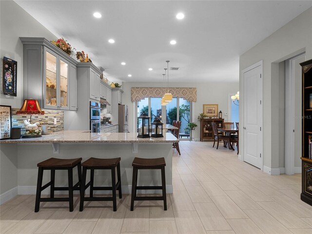 8818 Bismarck Palm Dr, Winter Garden, FL 34787 - kitchen with gray cabinetry, light stone counters, a peninsula, recessed lighting, and decorative backsplash