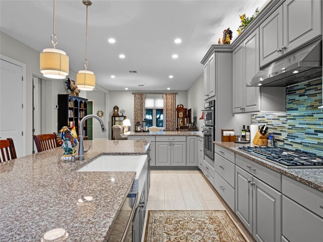 8818 Bismarck Palm Dr, Winter Garden, FL 34787 - kitchen featuring gray cabinetry, stainless steel appliances, under cabinet range hood, decorative backsplash, and light stone counters