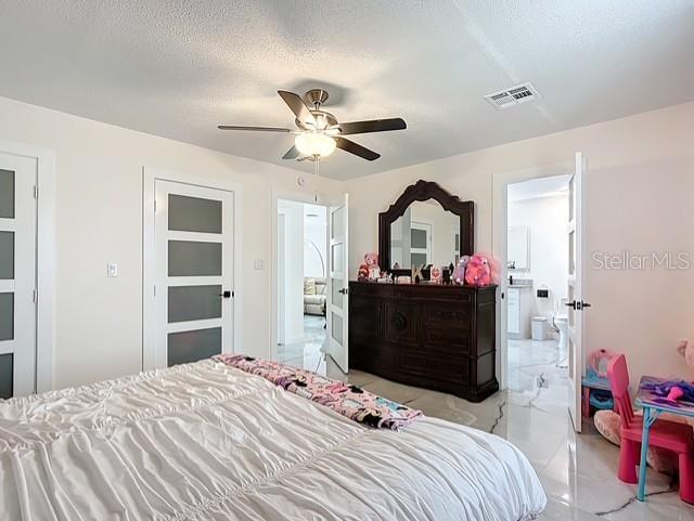 516 Petes Ln, Davenport, FL 33837 - bedroom featuring light marble finish flooring, a textured ceiling, ensuite bath, and ceiling fan